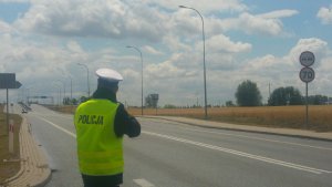 Zdjęcie pokazuje policjanta ruchu drogowego wykonującego pomiar prędkości pojazdu na drodze
