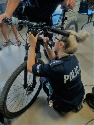 policjantka nanosi numer identyfikacyjny na ramę roweru a dzielnicowy przytrzymuje rower