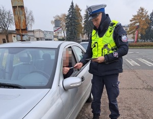Policjant ruchu drogowego podczas kontroli pojazdu przekazuje kierowcy ulotkę przez okno pojazdu